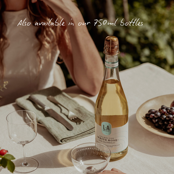 Bottle of white rose on a table with a glass and grapes, text indicating availability in 750ml bottles.