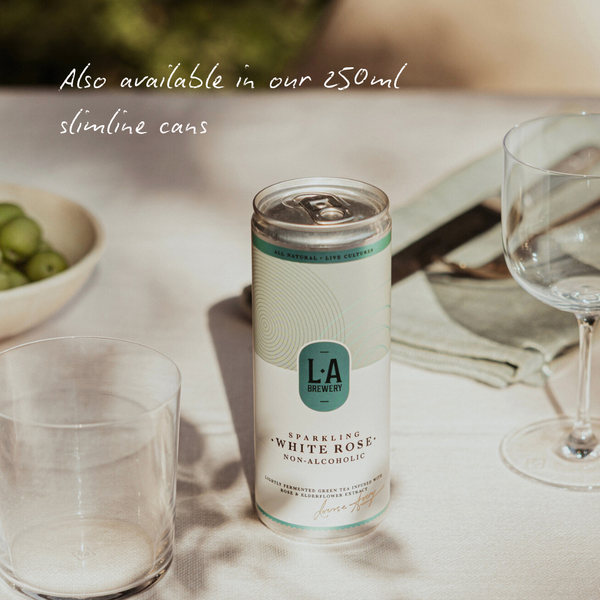 Can of L.A Brewery Sparkling White Rose non-alcoholic drink on a table with glasses and a bowl of grapes.